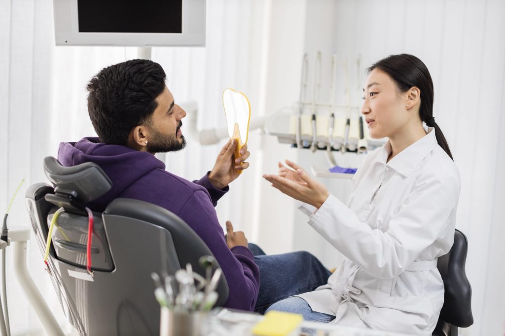 Portrait of handsome bearded male checking his teeth while looking at mirror after curing teeth.