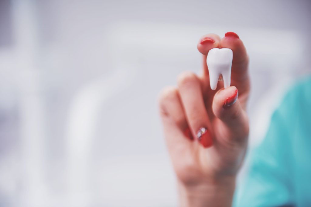 white tooth held in hand with red nails