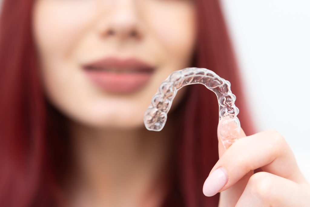 woman holding clear orthodontic aligner for teeth