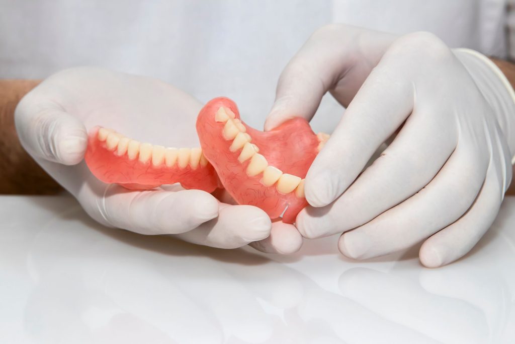 Gloved hands holding a set of full upper and lower dentures with pink acrylic gums