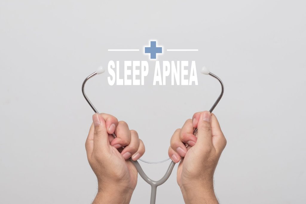 Hands holding a stethoscope beneath the words Sleep Apnea and a blue medical cross